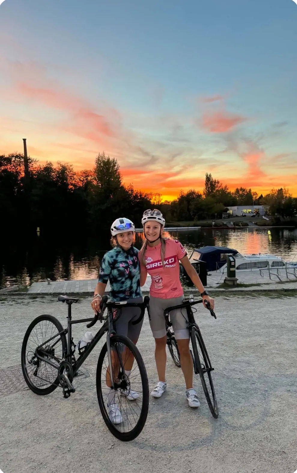 Deux cyclistes du collectif posent avec leurs vélos au bord de l'eau, au coucher du soleil